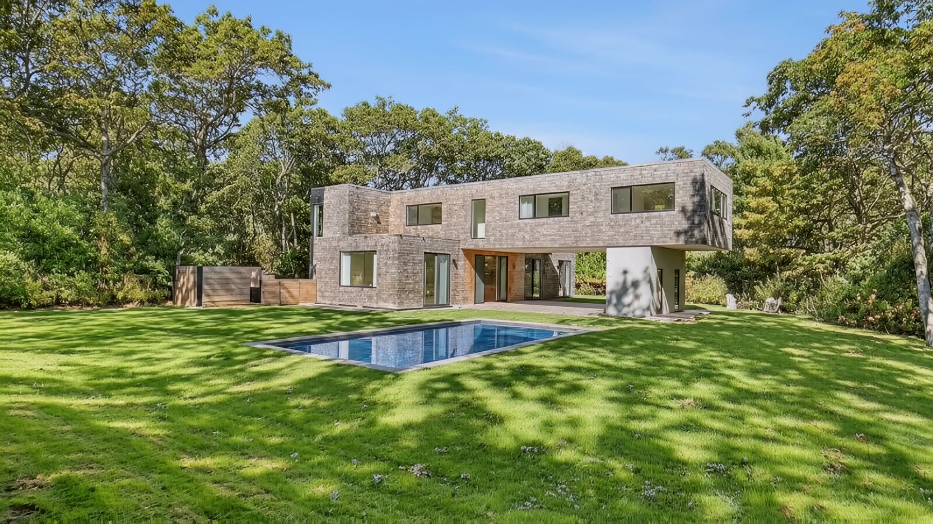 Modern cedar-shingled home with saltwater pool and manicured lawn on a sunny day